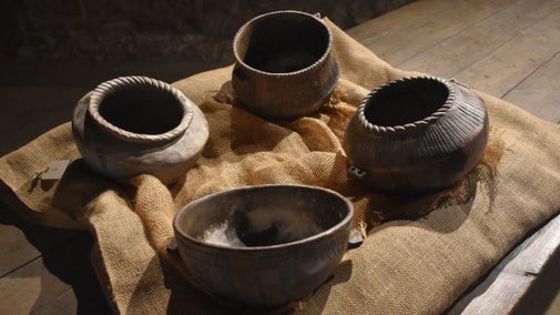 Four ceramic pots displayed on a large wooden table in the barn at Avebury.